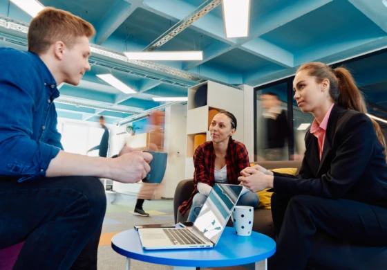 Colleagues talking over a laptop in a bright office breakout space