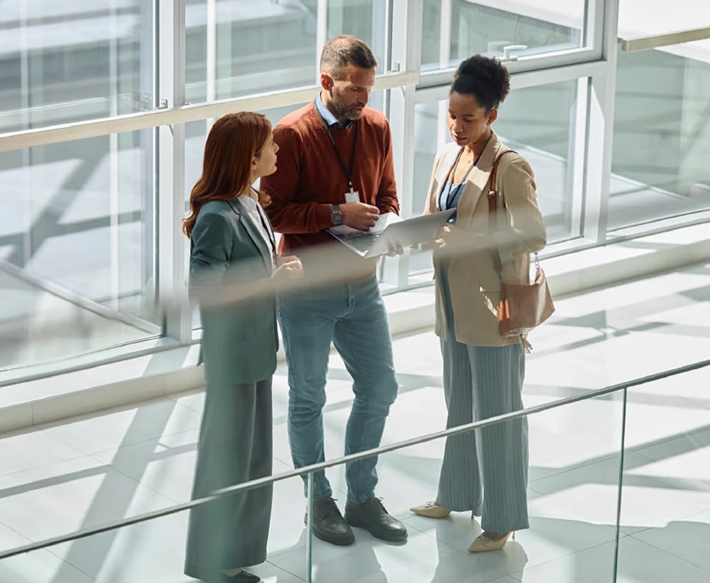 Three colleagues talking on a walkway in a glazed atrium